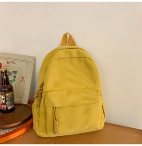Detail of yellow corduroy backpack featuring woven rope zippers and textured fabric