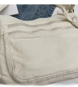 Detail of off-white canvas tote bag featuring multi-layer zippers and woven fabric texture