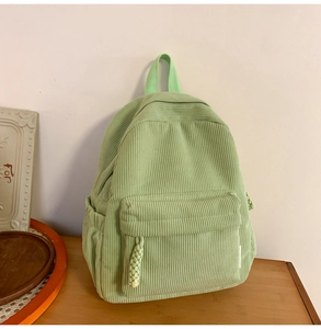 Detail view of a pale green corduroy backpack with side pocket and woven rope zipper pull