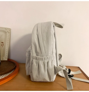 Detail of light gray corduroy backpack side pocket with elastic and adjustable strap