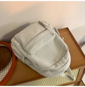 Detail of light grey corduroy backpack featuring woven rope handle on wooden cabinet
