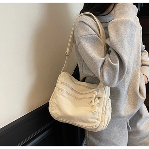 Detail of minimalist cream canvas tote bag showing multiple zipper pockets on model side