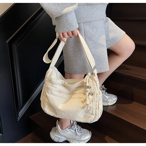 Detail of off-white canvas tote bag with multi-zipper pockets and wide shoulder strap