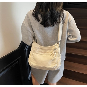 Detail of cream canvas tote bag showing multiple zipper pockets and wide strap on model