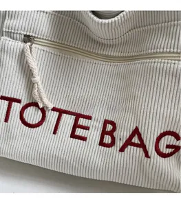 Detail der weißen Cord-Tragetasche mit roter Stickerei und hochwertigem Metallreißverschluss