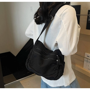 Close-up of black canvas tote bag showing multiple functional zipper pockets and strap