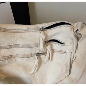 Close-up of multi-pocket cream canvas tote bag showing durable zippers and fabric texture