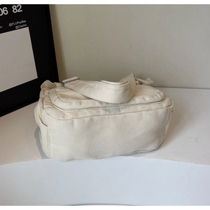 Detail of off-white canvas tote bag featuring flap zipper closure and wide strap