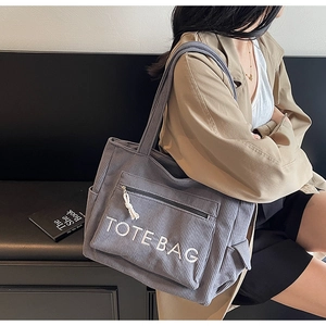 Detail der grau-blauen Cord-Einkaufstasche mit Logo, getragen von einem Model