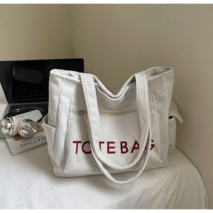 Detailansicht einer beigen Cord-Tragetasche mit roter Stickerei neben Lifestyle-Requisiten
