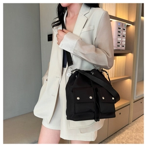 Detail of black nylon drawstring bucket bag with double front pockets on female model