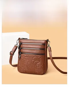 Detail of a brown leather crossbody bag featuring three zipper pockets and embossed roses