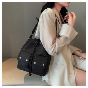 Detail view of a black nylon drawstring bucket bag with dual front pockets on a model