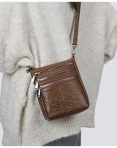 Detail of a brown embossed crossbody bag with rose pattern and multiple zippers on model
