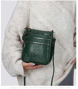 Close-up of dark green leather shoulder bag with embossed rose and triple zippers