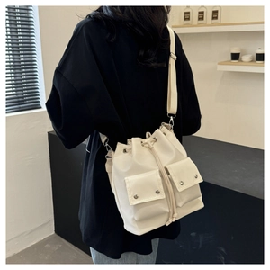 Detail view of cream nylon bucket bag with dual front pockets and adjustable strap