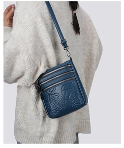 Detail of navy blue leather crossbody bag with rose embossed pattern and triple zippers