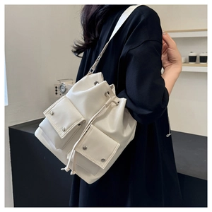 Detail of cream drawstring bucket bag with metallic snap pockets and wide shoulder strap