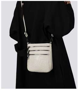 Detail of white embossed floral crossbody bag with three metal zipper compartments