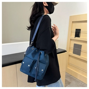Deep blue nylon drawstring bucket bag with dual front pockets worn by a model
