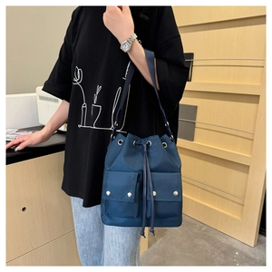 Detail of blue nylon drawstring bucket bag featuring front flap pockets and woven strap