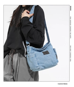 Detailed view of light blue denim crossbody bag featuring a brown leather patch and woven label