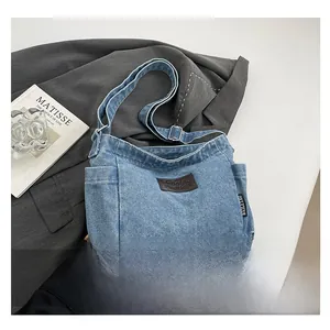 Detail of blue denim crossbody bag featuring a brown leather patch and adjustable strap