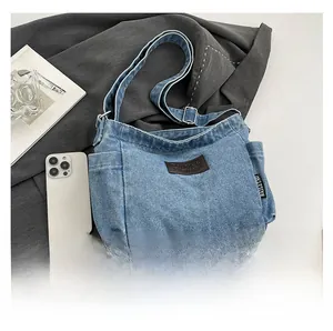 Detail view of denim crossbody bag showing adjustable strap and brown leather patch