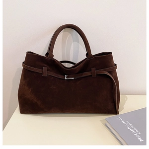 Close-up of a coffee brown suede tote bag with decorative leather strap and metal buckle