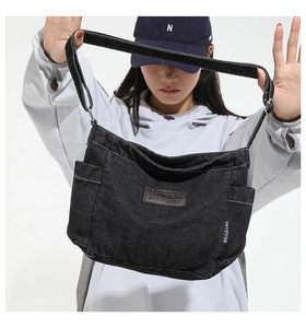 Detailed view of black denim shoulder bag featuring front pockets and leather logo patch