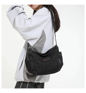 Close-up of black denim shoulder bag featuring leather logo patches and washed texture