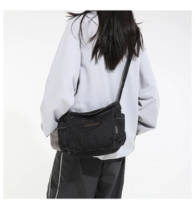 Close-up of black denim crossbody bag with side woven label and leather logo patch