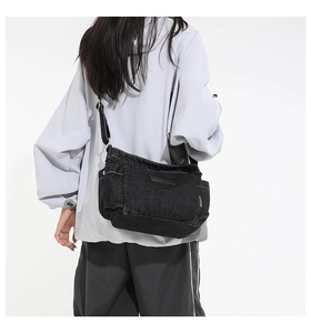 Detail of black denim messenger bag with adjustable strap and vintage leather logo patch