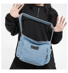 Detail of light blue denim crossbody bag featuring leather patch and wide shoulder strap