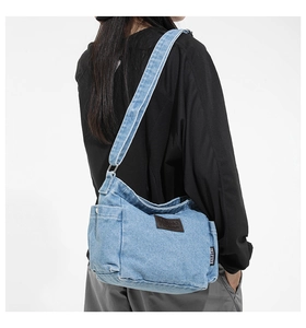 Detail of light blue denim crossbody bag featuring a vintage leather patch and side label