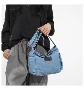 Detail of light blue denim crossbody bag featuring brown leather patch and side pocket