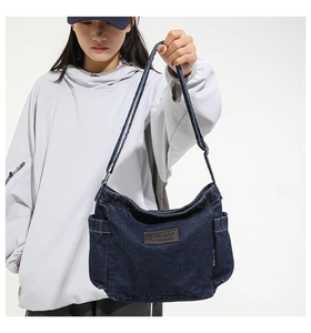 Detailed close-up of dark blue denim shoulder bag featuring a brown leather logo patch