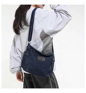 Detail view of a vintage dark blue denim crossbody bag with brown faux leather patch
