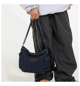Detail of dark blue denim crossbody bag with brown leather patch and side pockets