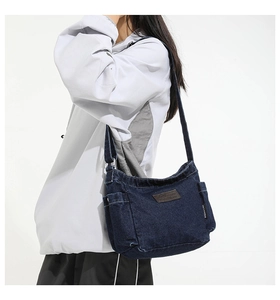 Detail of navy blue denim crossbody bag with adjustable strap and leather logo patch