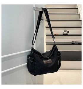 Detail of black denim tote bag showing white contrast stitching and side pocket design