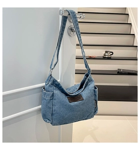 Detail of blue denim hobo bag featuring brown leather patch and side pocket on door