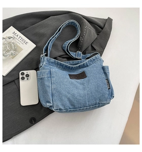 Detail of light blue denim crossbody bag featuring a leather logo patch and adjustable strap