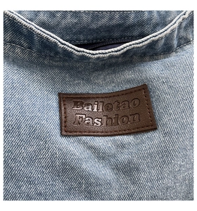 Close-up of blue denim shoulder bag with brown leather brand patch and zipper detail
