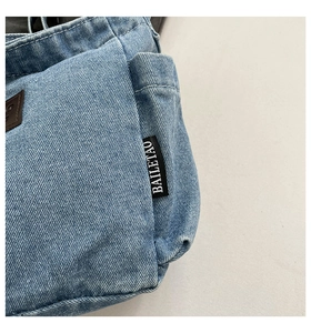 Close-up of light blue denim fabric texture and black logo label on the shoulder bag