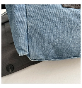 Close-up of blue denim fabric texture and brown leather label on a shoulder bag