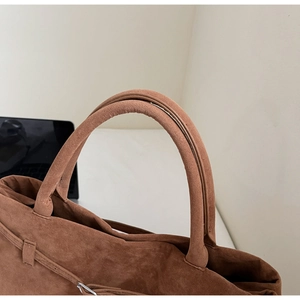 Detail of caramel suede tote bag featuring rounded top handles and soft matte texture