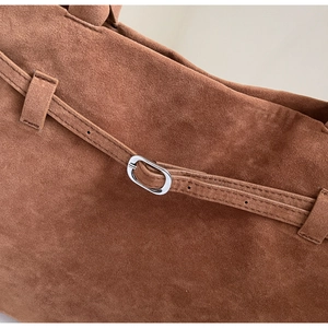 Close-up of caramel suede tote bag featuring silver metal oval buckle and fine stitching