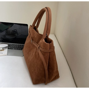 Detail of a brown suede tote bag featuring a leather side buckle and spacious interior