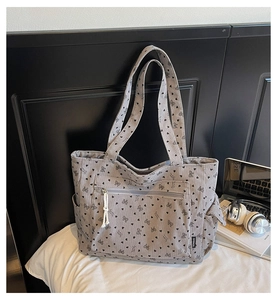 Close-up of gray corduroy tote bag featuring black heart patterns and front zipper pocket